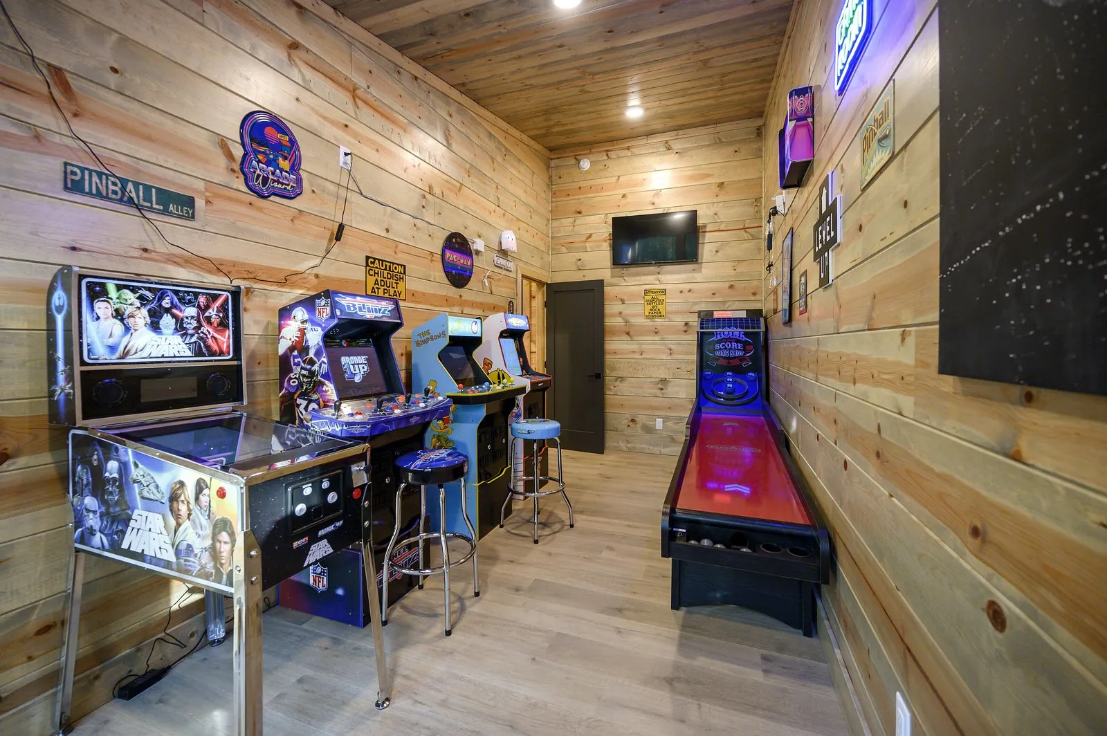 Arcade room at The Avalon with pinball machine, arcade cabinets, skee-ball, and neon signs on knotty pine walls